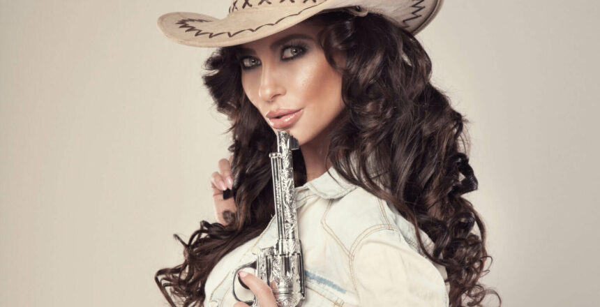 Portrait of sexy brunette cowgirl with revolver, looking at camera.